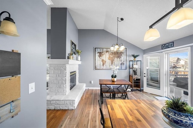 dining space featuring a fireplace, lofted ceiling, wood finished floors, a chandelier, and baseboards