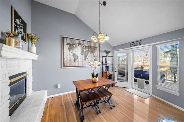 dining space with a fireplace, vaulted ceiling, wood finished floors, a chandelier, and baseboards