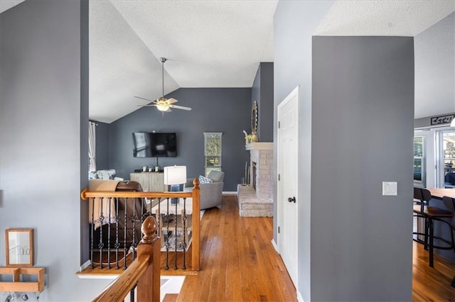 hallway featuring lofted ceiling, light wood-style flooring, an upstairs landing, and a textured ceiling