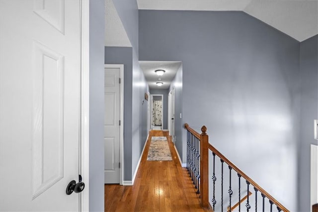 hall featuring lofted ceiling, baseboards, an upstairs landing, and wood finished floors