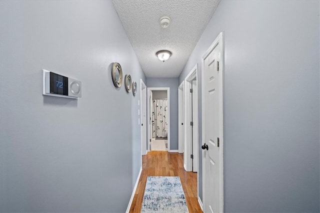 hall featuring a textured ceiling, light wood finished floors, and baseboards