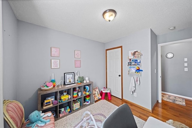 playroom with a textured ceiling, baseboards, and wood finished floors