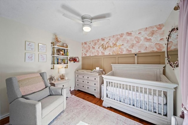 bedroom featuring wallpapered walls, a ceiling fan, wood finished floors, and wainscoting