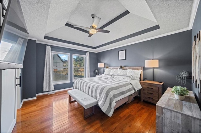 bedroom featuring crown molding, a textured ceiling, a raised ceiling, and dark wood finished floors