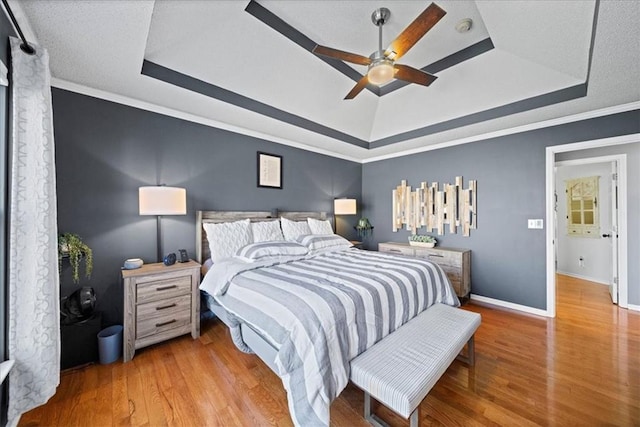 bedroom featuring a ceiling fan, baseboards, light wood finished floors, a raised ceiling, and crown molding