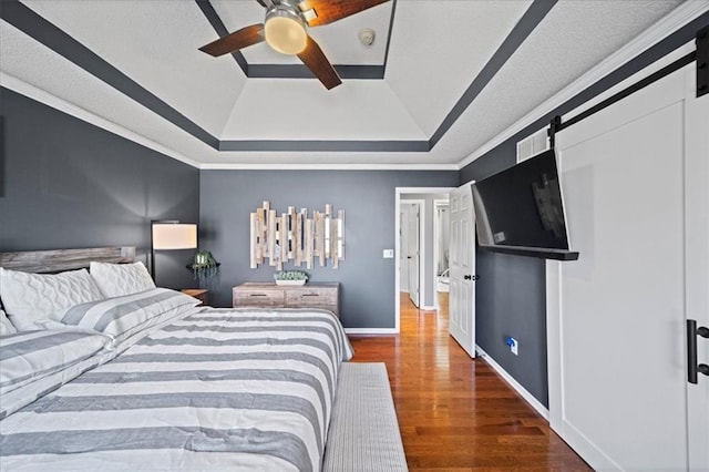 bedroom featuring a tray ceiling, visible vents, a barn door, wood finished floors, and baseboards