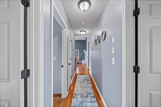 hallway with light wood-style floors, baseboards, and a textured ceiling