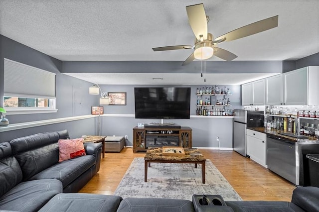 living area with ceiling fan, a textured ceiling, a bar, baseboards, and light wood finished floors