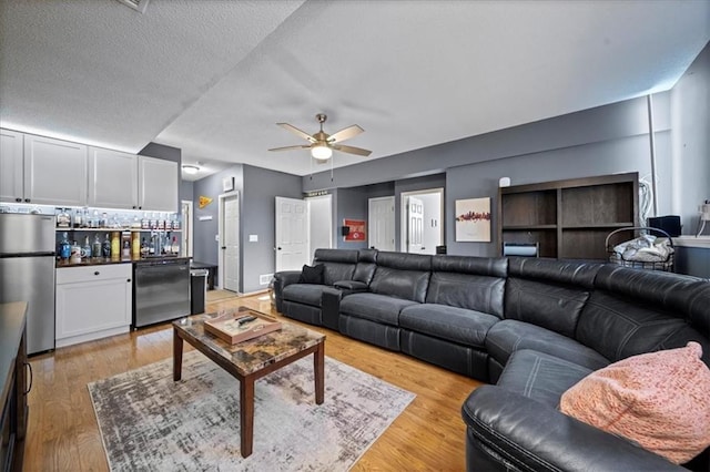 living area featuring light wood finished floors, a dry bar, a textured ceiling, and a ceiling fan