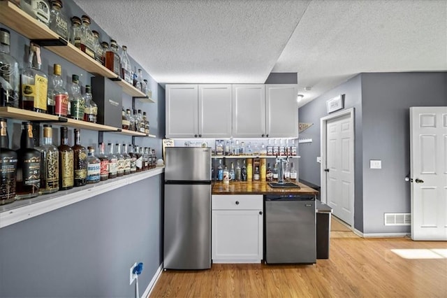 bar featuring light wood finished floors, visible vents, bar, stainless steel appliances, and a textured ceiling