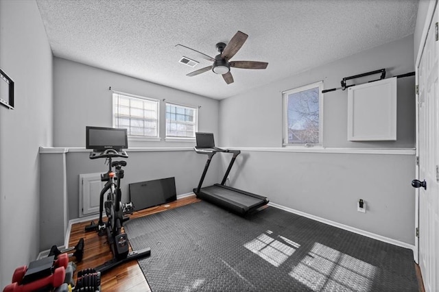 workout area featuring a textured ceiling, wood finished floors, a ceiling fan, visible vents, and baseboards