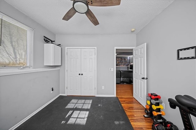 interior space featuring a closet, a ceiling fan, a textured ceiling, wood finished floors, and baseboards