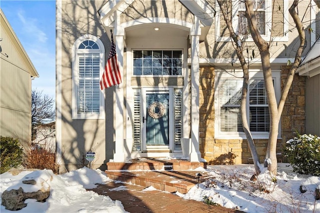 snow covered property entrance featuring stone siding