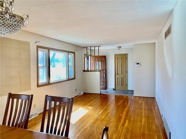 unfurnished dining area with visible vents, a textured ceiling, and wood finished floors