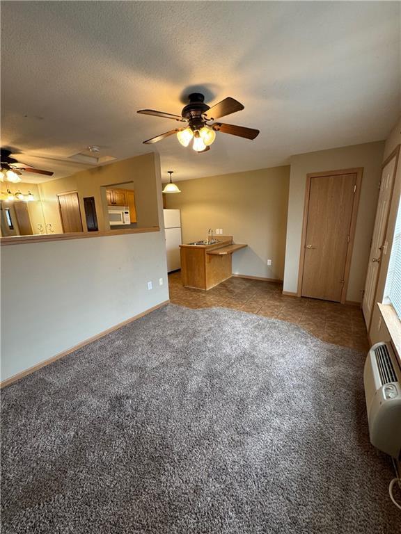 unfurnished living room with a textured ceiling, light carpet, sink, and ceiling fan