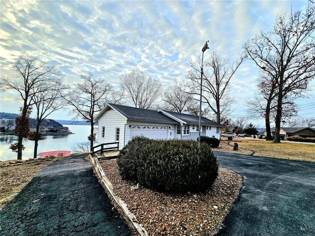 view of home's exterior featuring an attached garage, aphalt driveway, and a water view