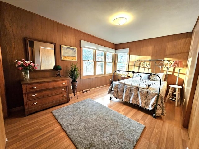 bedroom featuring light wood-type flooring, wood walls, and visible vents