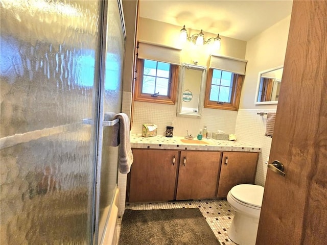 full bath featuring toilet, a wainscoted wall, an enclosed shower, vanity, and tile walls