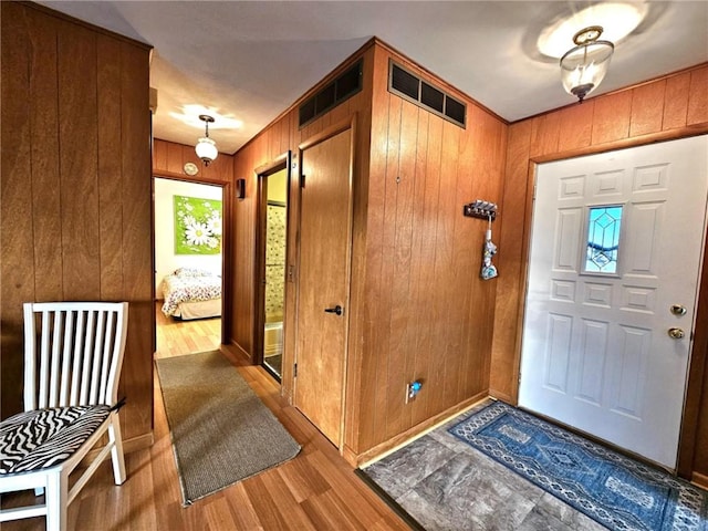 foyer entrance with wooden walls, visible vents, and light wood-style floors