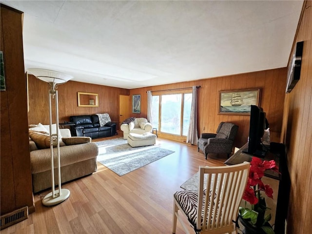 living room with light wood finished floors, visible vents, and wooden walls