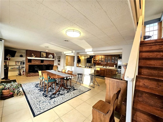 dining room with built in features, a brick fireplace, stairway, and light tile patterned floors