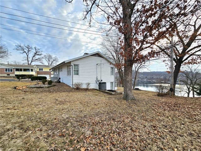 view of side of home featuring a water view, a lawn, and central AC unit