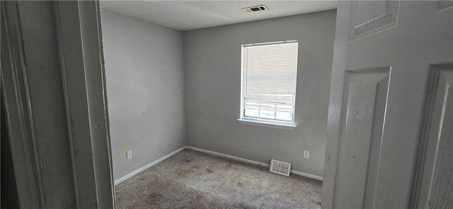 spare room with light carpet, a textured ceiling, visible vents, and baseboards