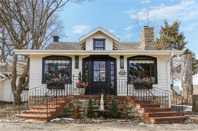 bungalow-style home featuring a chimney and roof with shingles