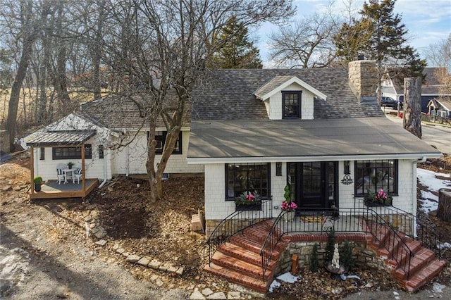 view of front facade with a chimney, a porch, and roof with shingles