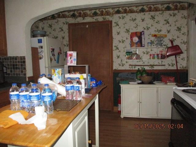 kitchen featuring freestanding refrigerator, a wainscoted wall, arched walkways, and wallpapered walls