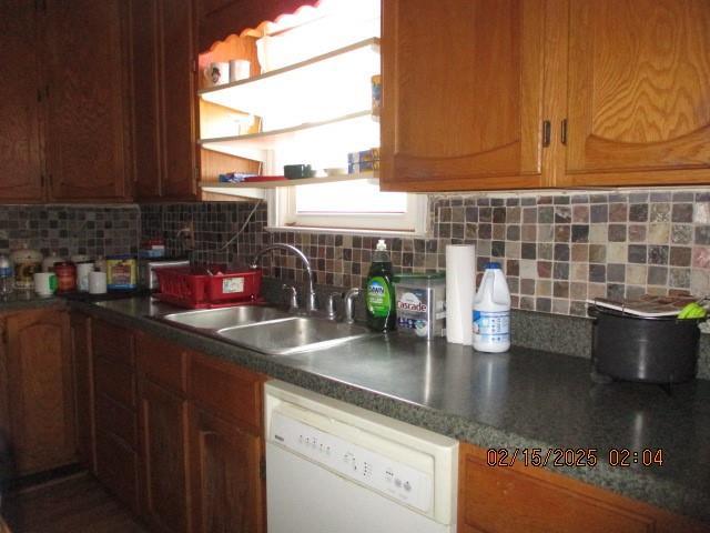 kitchen with decorative backsplash, dark countertops, white dishwasher, open shelves, and a sink