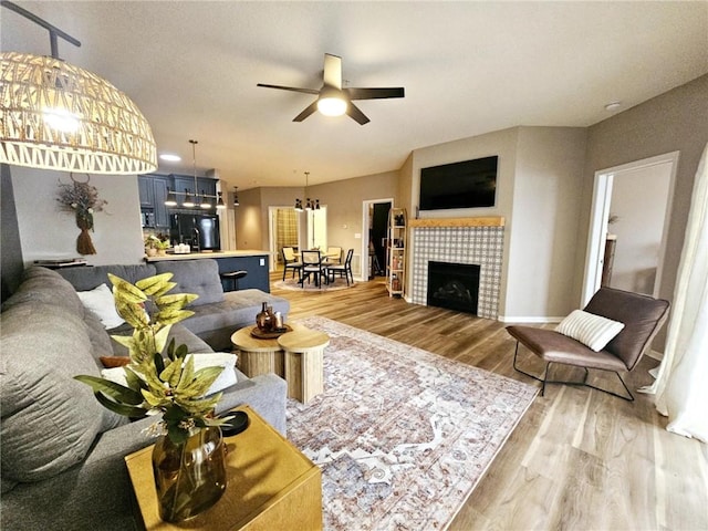 living room featuring a ceiling fan, wood finished floors, and a tile fireplace