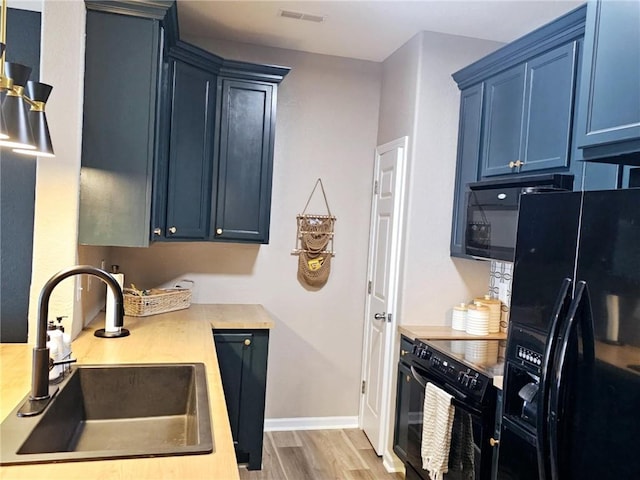 kitchen featuring visible vents, light wood-style floors, a sink, blue cabinets, and black appliances