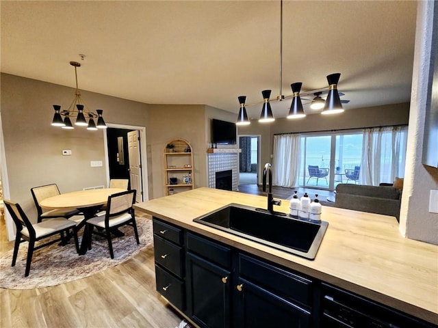 kitchen featuring a fireplace, a sink, open floor plan, light wood-type flooring, and pendant lighting