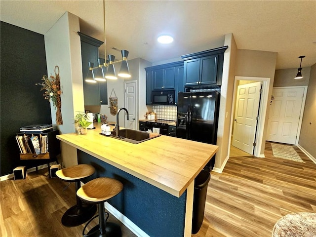 kitchen featuring a breakfast bar, a peninsula, blue cabinets, hanging light fixtures, and black appliances