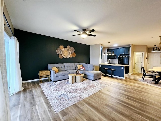 living area with ceiling fan with notable chandelier, wood finished floors, and baseboards