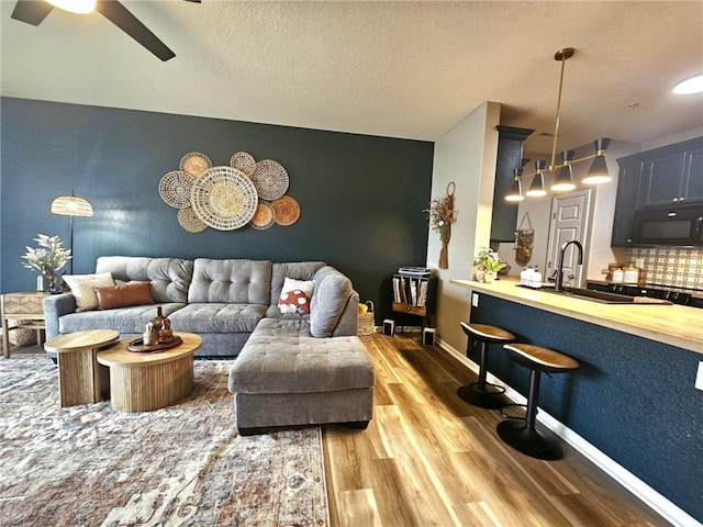 living room with a ceiling fan, a textured ceiling, baseboards, and wood finished floors