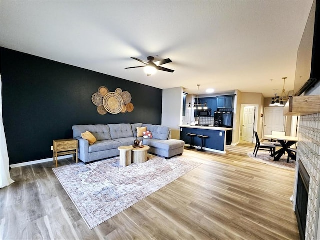 living area featuring ceiling fan with notable chandelier, an accent wall, wood finished floors, and baseboards