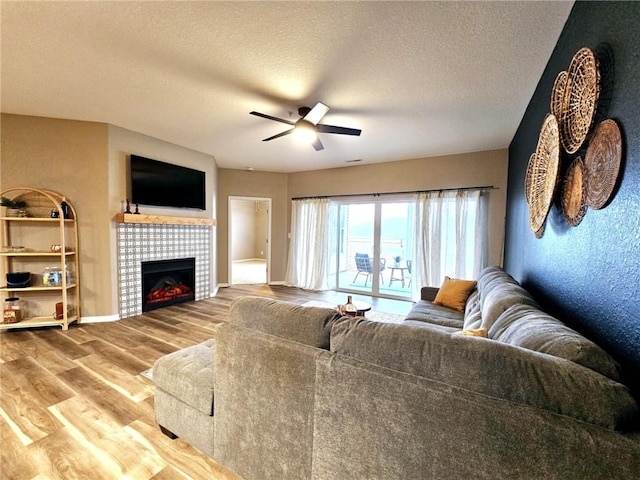 living room with a tile fireplace, ceiling fan, a textured ceiling, and wood finished floors