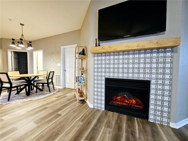 interior space with baseboards, visible vents, a tiled fireplace, wood finished floors, and vaulted ceiling