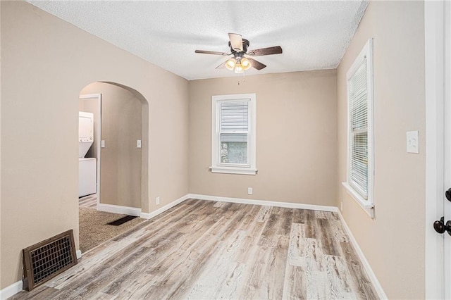 unfurnished room featuring ceiling fan, light wood-type flooring, stacked washer / drying machine, and a textured ceiling