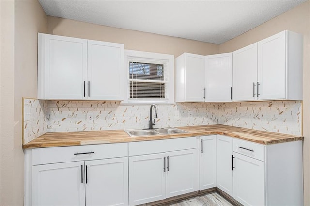 kitchen with wood counters, sink, backsplash, light wood-type flooring, and white cabinets