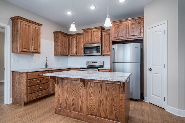 kitchen with sink, light stone counters, a center island, decorative light fixtures, and stainless steel appliances