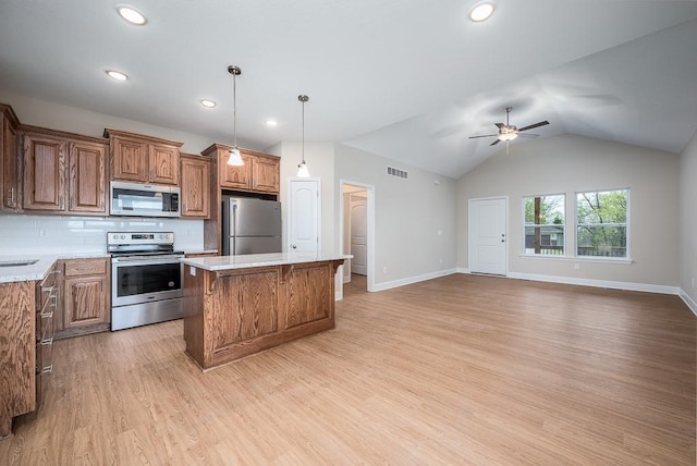 kitchen featuring hanging light fixtures, light hardwood / wood-style flooring, a kitchen island, tasteful backsplash, and appliances with stainless steel finishes