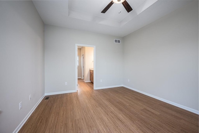 empty room featuring a raised ceiling, light hardwood / wood-style flooring, and ceiling fan