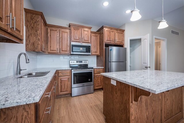 908 2nd St, Perry, KS 66073 - kitchen with appliances with stainless steel finishes, a sink, brown cabinetry, light wood-style flooring, and lofted ceiling