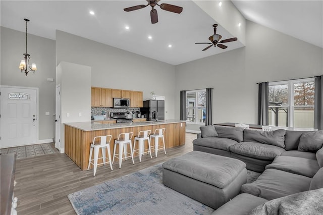 living room with ceiling fan with notable chandelier, high vaulted ceiling, light wood finished floors, and baseboards