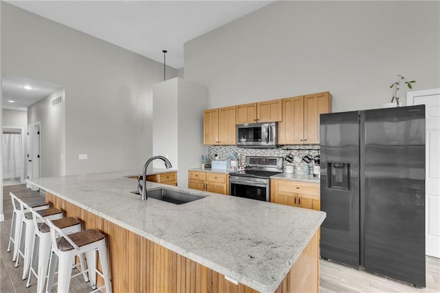 kitchen featuring a breakfast bar area, stainless steel appliances, backsplash, a sink, and light stone countertops