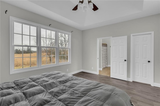 bedroom with a tray ceiling, baseboards, ceiling fan, and wood finished floors