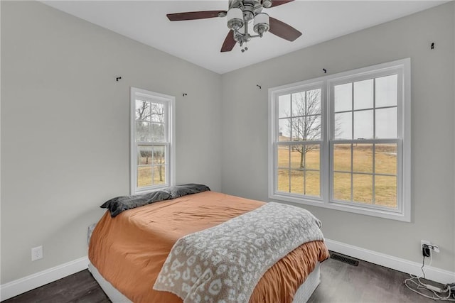 bedroom featuring a ceiling fan, dark wood-style flooring, visible vents, and baseboards